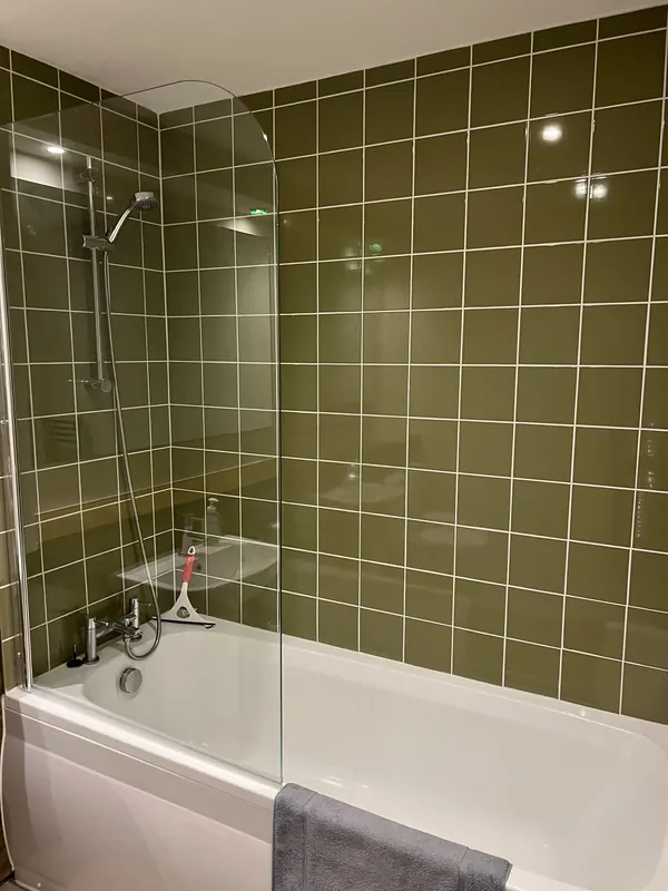 Bath with a glass shower screen and walls tiled in olive green square tiles