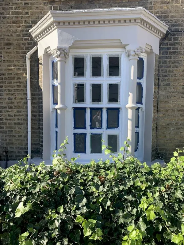 White-painted bay window with decorative columns on a yellow brick house