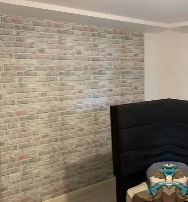Bedroom wall papered in a brick-effect design behind a black headboard